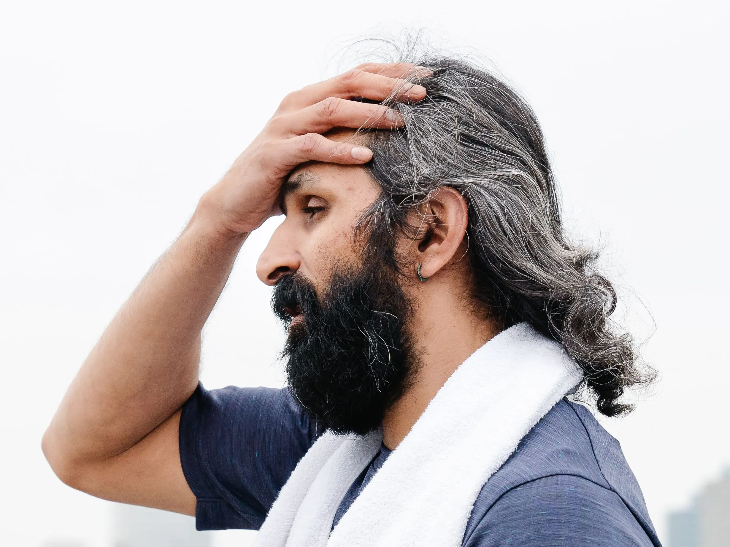 Man with a towel around his neck holding his hand to his forehead after a workout, a picture of the fatigue common with low testosterone