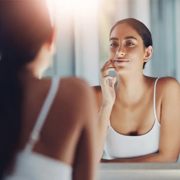 A woman examining her skin closely in the mirror