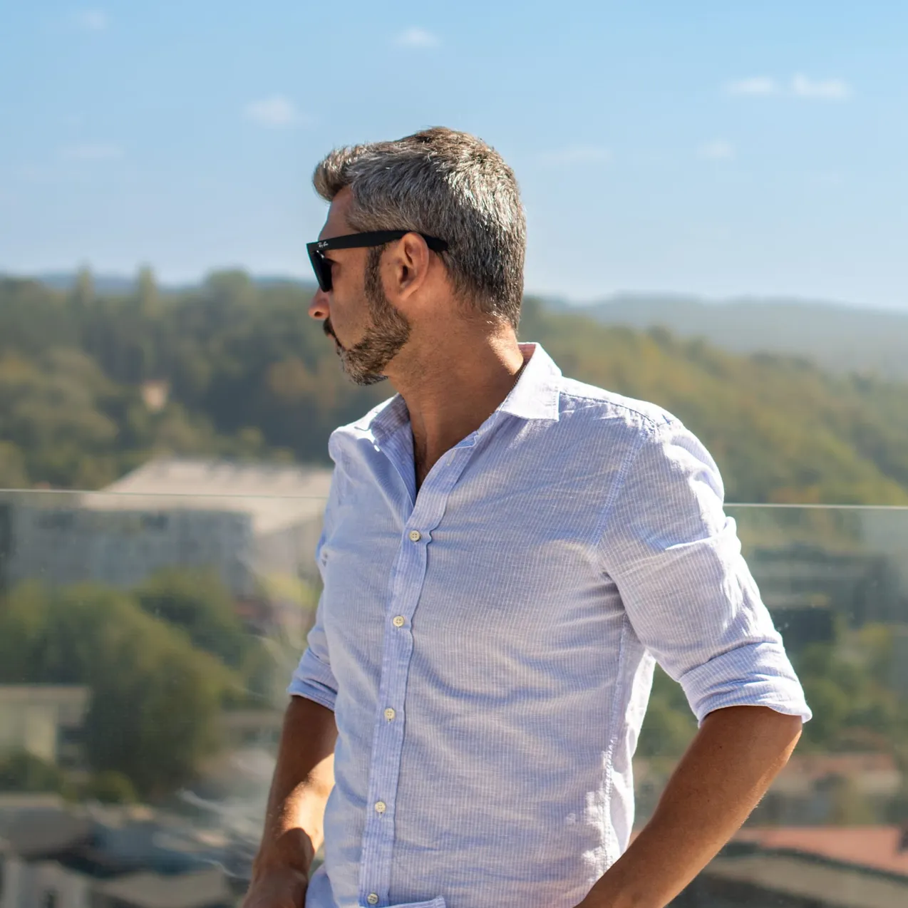 Man in a linen shirt and sunglasses standing on a sunlit terrace