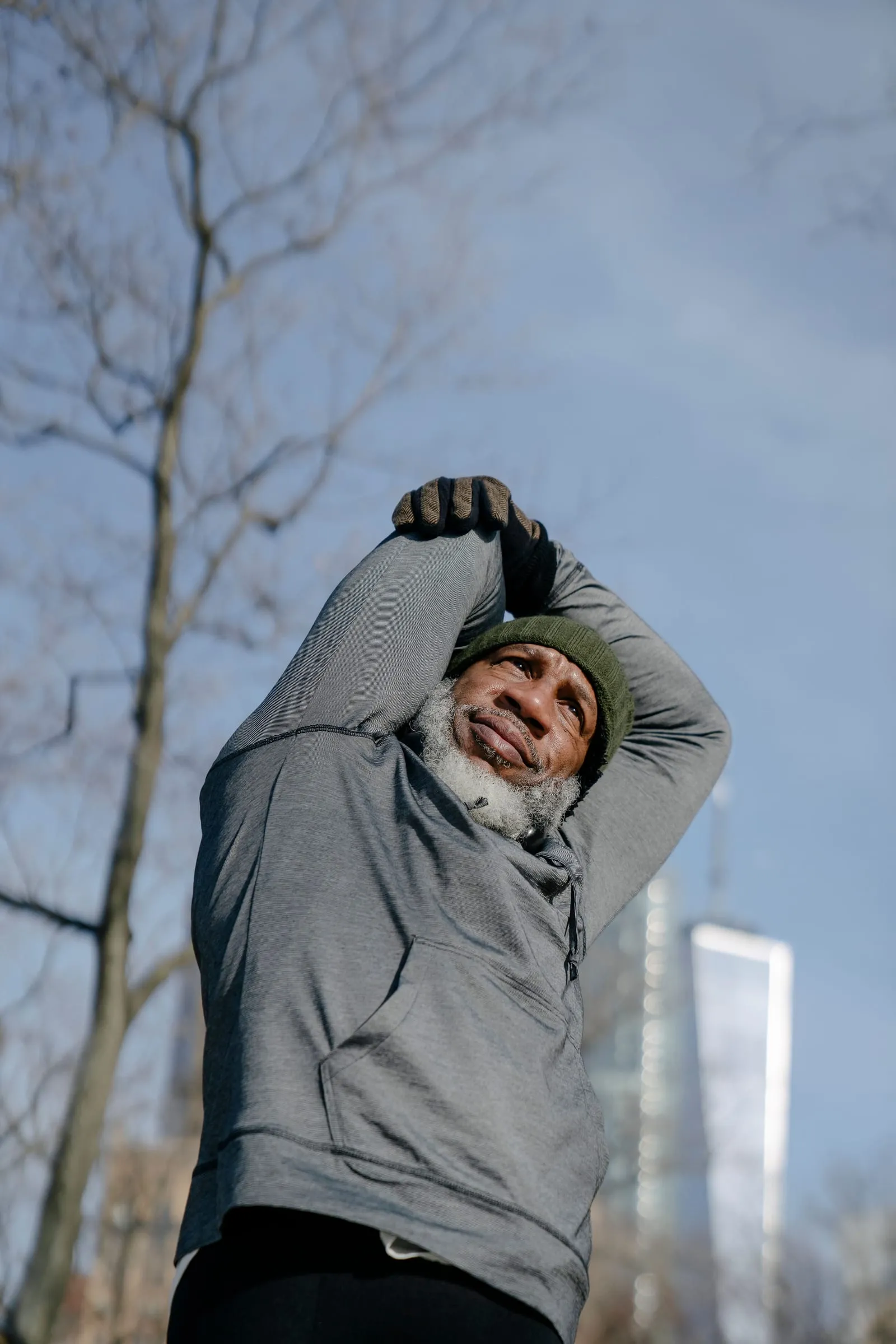 Older man with a gray beard stretching his arms overhead before exercising outdoors