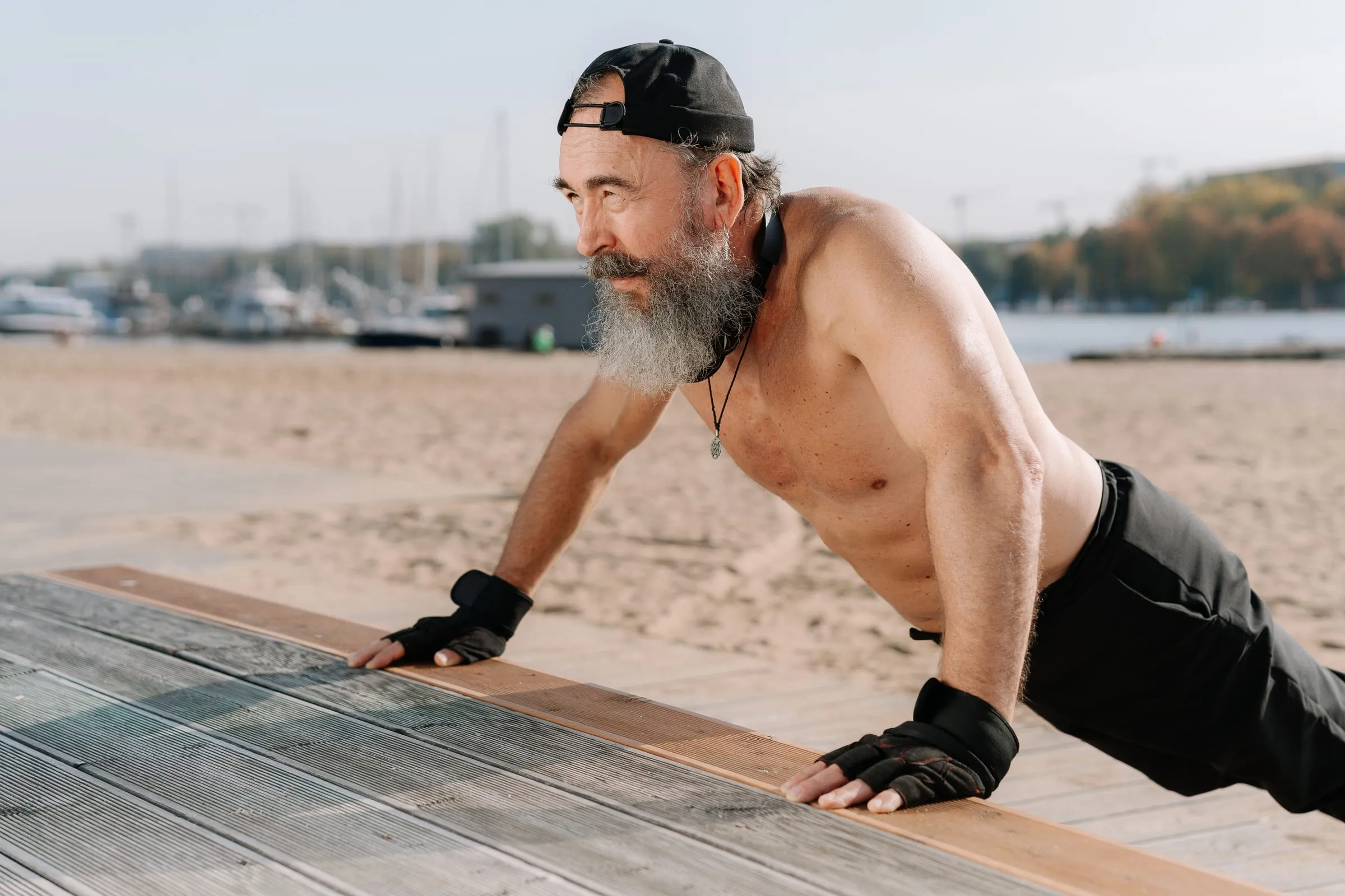 Gray-bearded man doing incline push-ups on a boardwalk by the beach