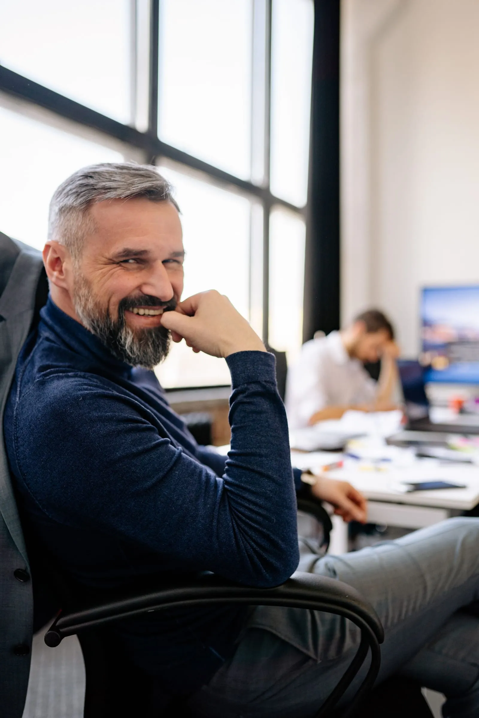 Smiling gray-haired man with a beard sitting in an office chair