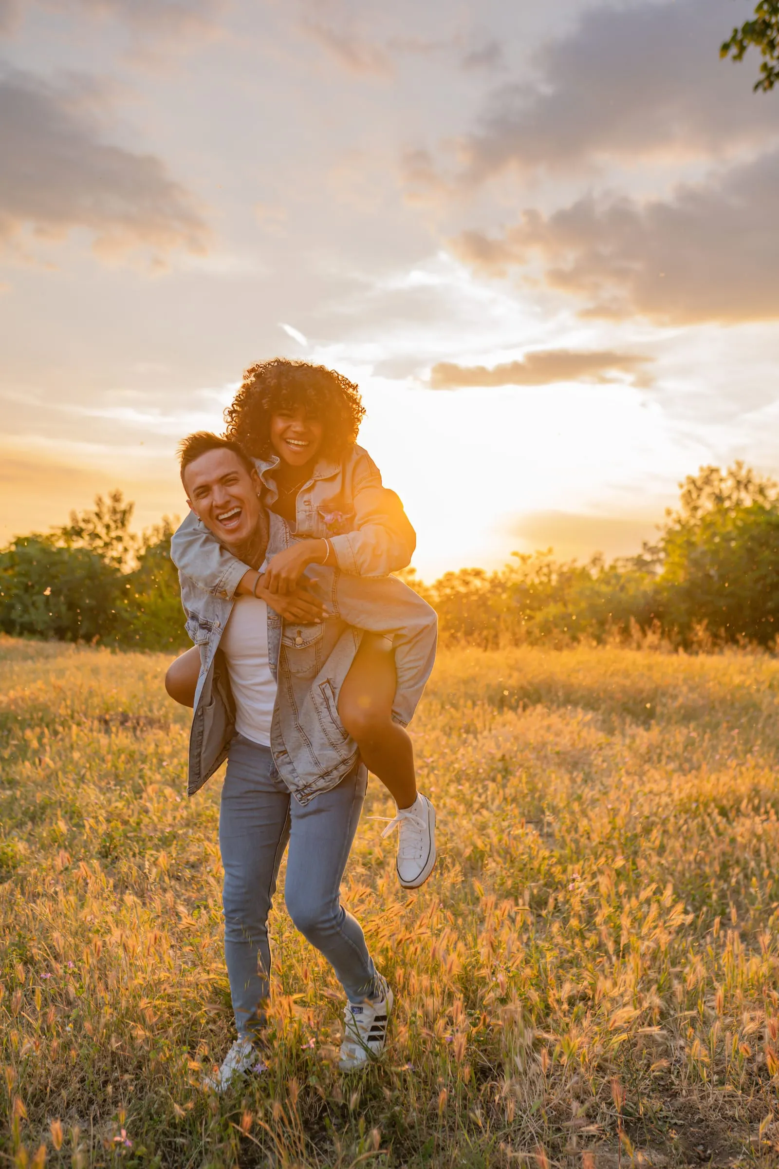 Smiling couple outdoors at sunset, the woman riding on the man's back