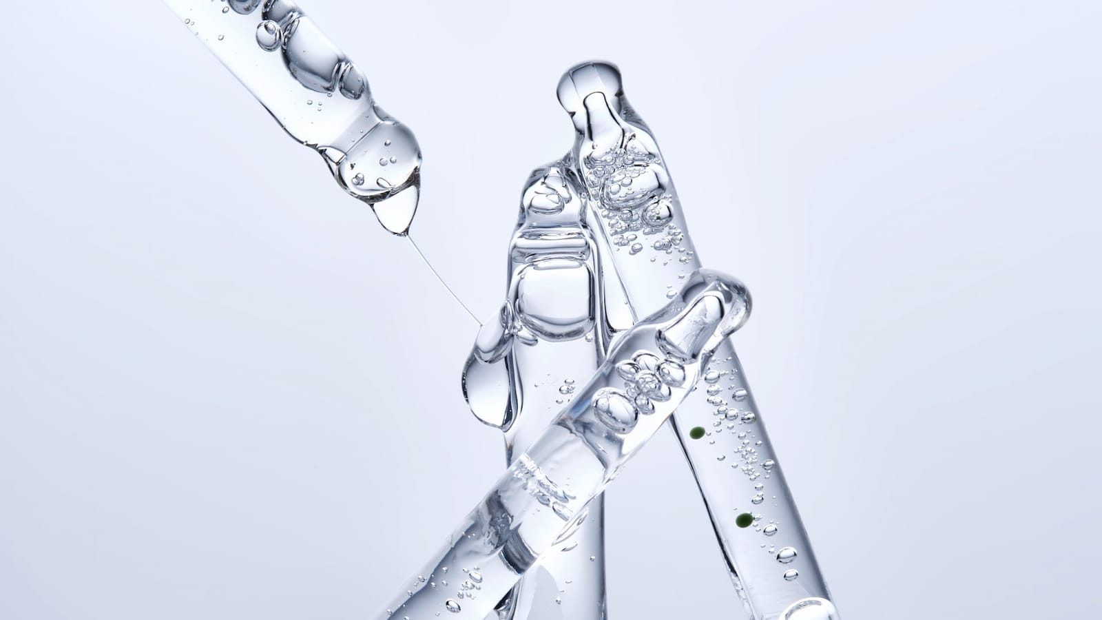 Clear serum droplet falling from a glass pipette above crossed glass applicators, representing precise injectable dosing.